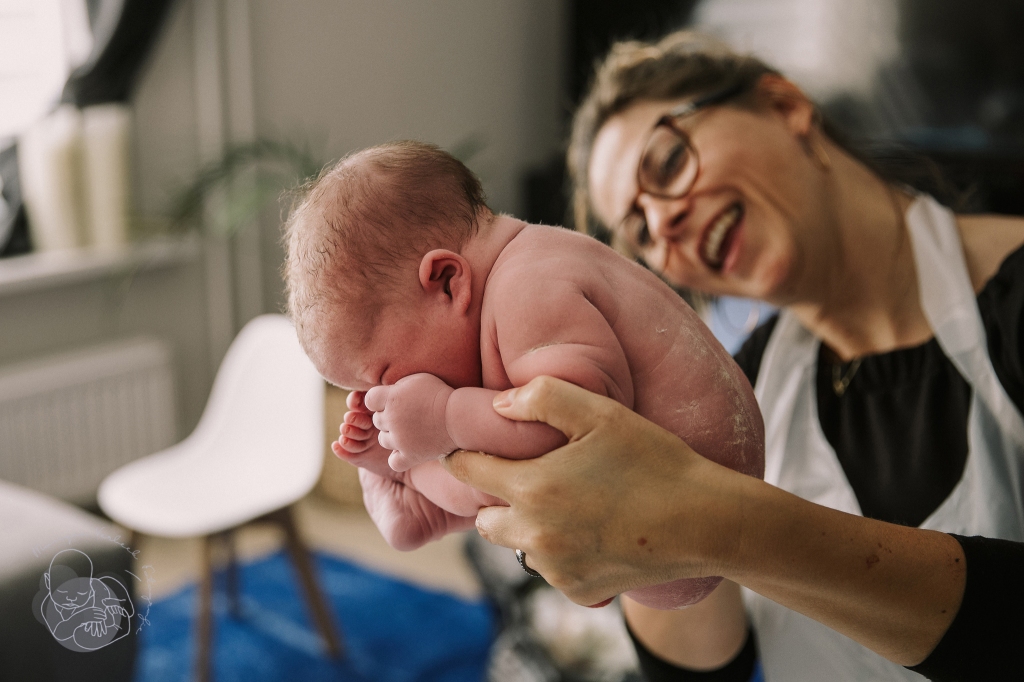 Verloskundige houdt pasgeboren baby omhoog